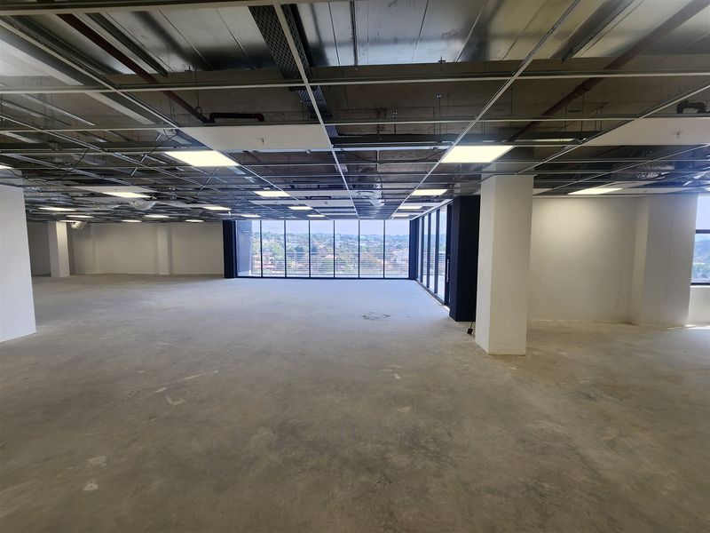 A spacious, open-plan office area featuring floor-to-ceiling windows with panoramic views, exposed structural columns, and an unfinished ceiling grid ready for final fit-out.