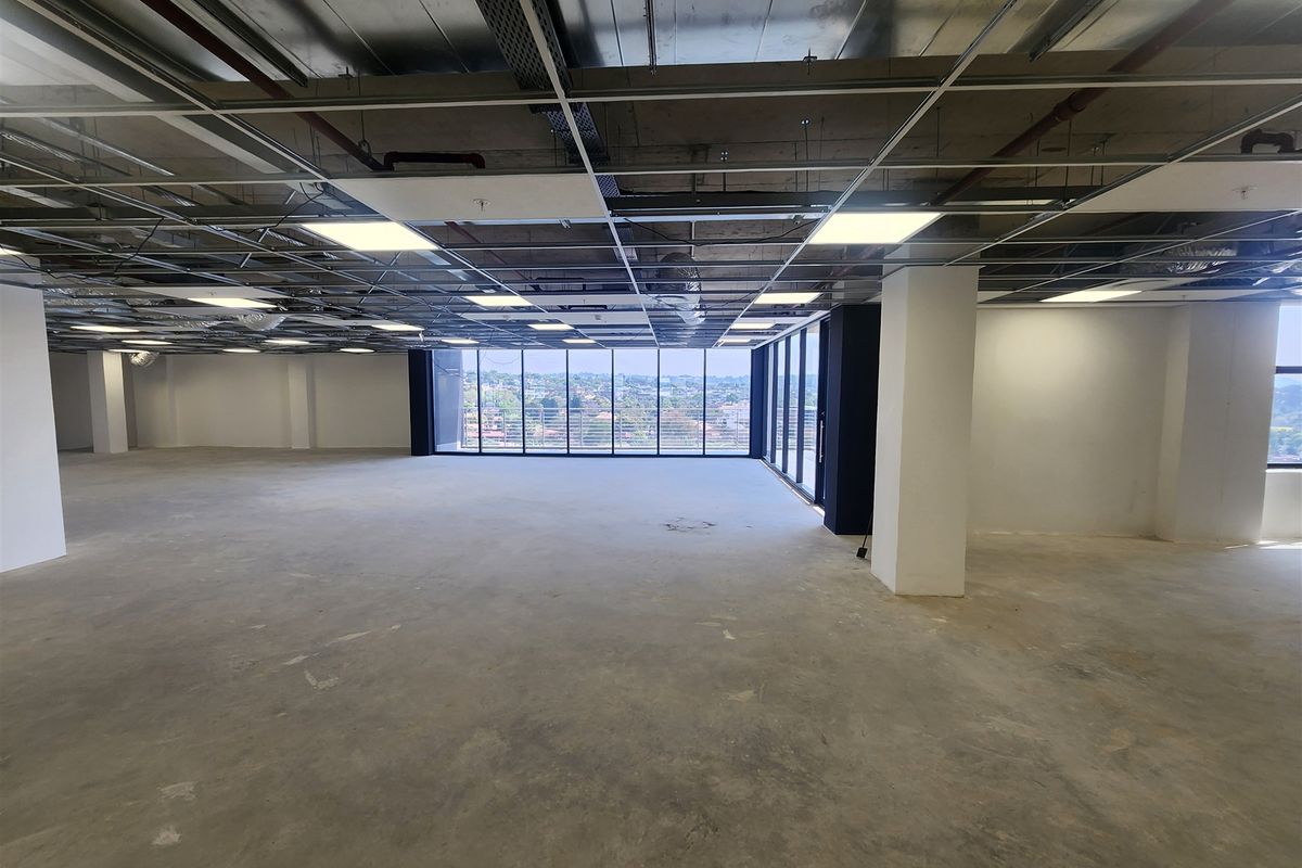 A spacious, open-plan office area featuring floor-to-ceiling windows with panoramic views, exposed structural columns, and an unfinished ceiling grid ready for final fit-out.