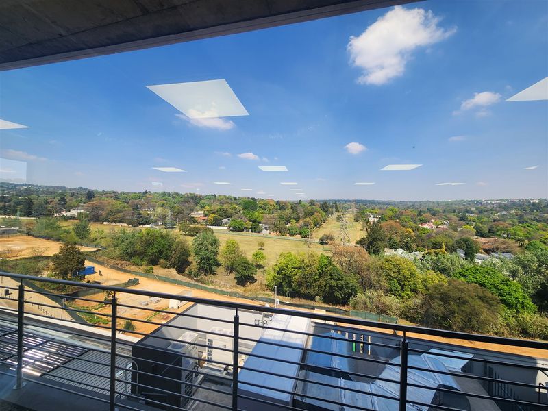 Elevated panoramic view overlooking a green suburban landscape and surrounding area, captured from a modern office building with a metal balustrade.