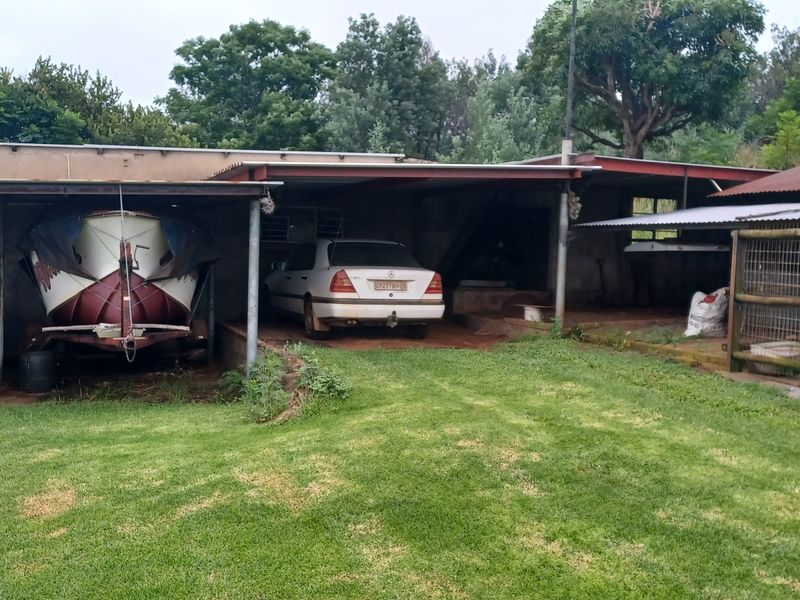 Open-sided farm garage structure with corrugated metal roofing, concrete flooring, and an adjacent fenced enclosure, suitable for vehicle and equipment storage.