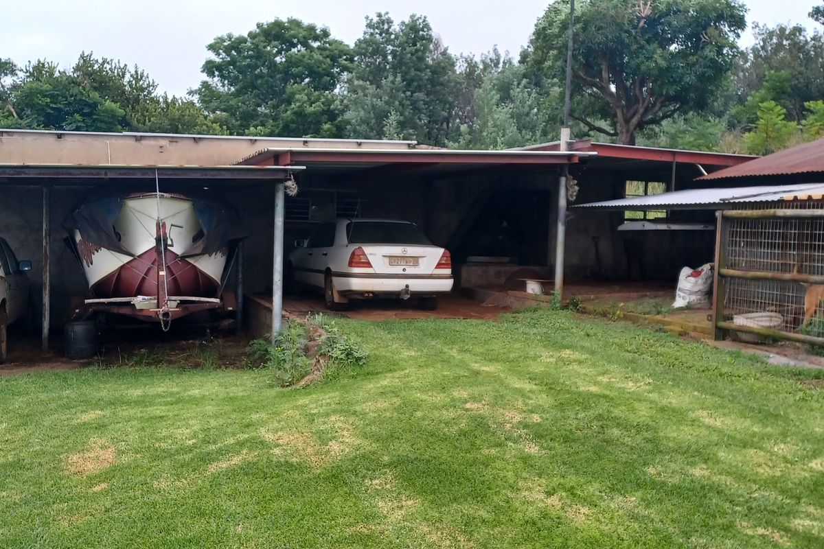 Open-sided farm garage structure with corrugated metal roofing, concrete flooring, and an adjacent fenced enclosure, suitable for vehicle and equipment storage.