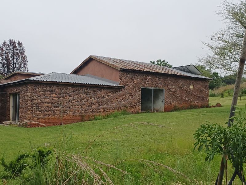 Rear view of a rustic brick farmhouse featuring a corrugated metal roof and sliding glass door access set within a large grassy field.