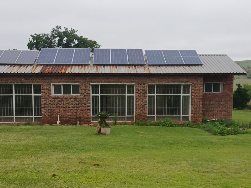 A rear view of a face brick farm building featuring a corrugated metal roof equipped with solar panels and large windows with security bars.