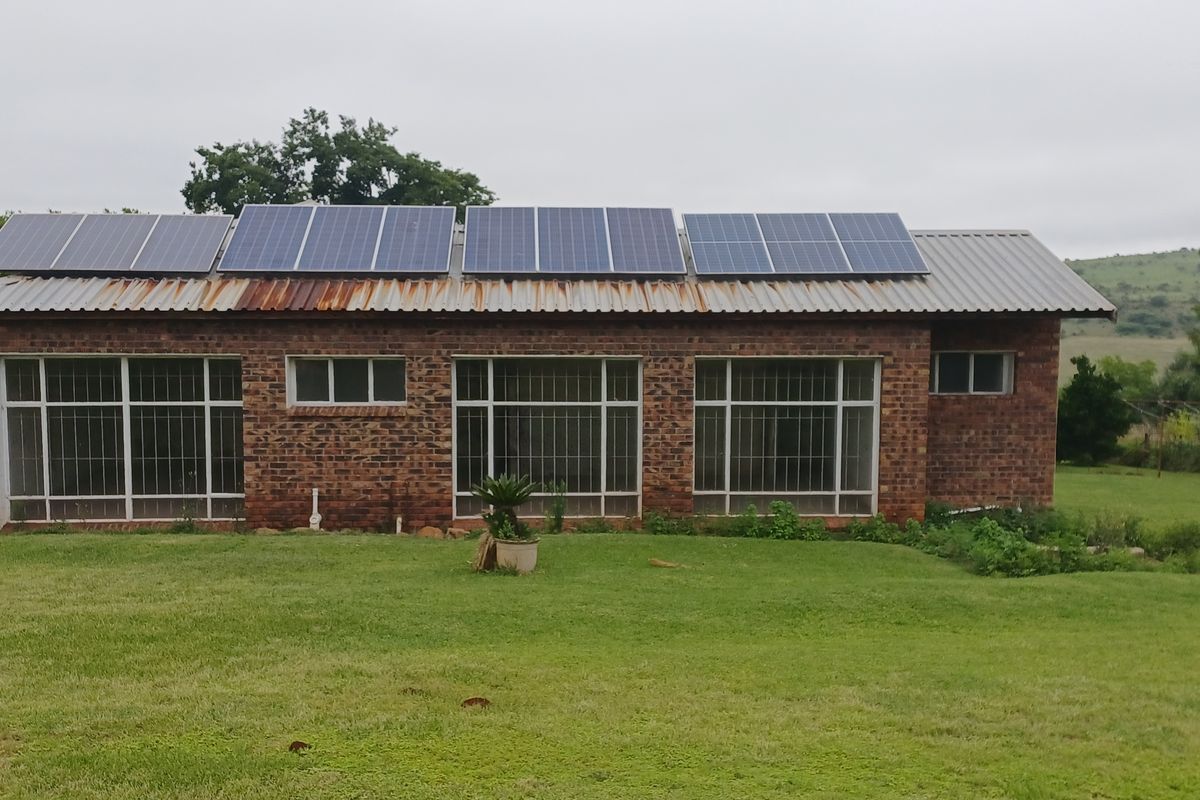A rear view of a face brick farm building featuring a corrugated metal roof equipped with solar panels and large windows with security bars.
