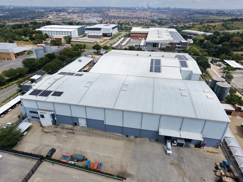 Aerial view of a large industrial warehouse facility featuring a metal roof with solar panels, paved parking, and secure perimeter access.