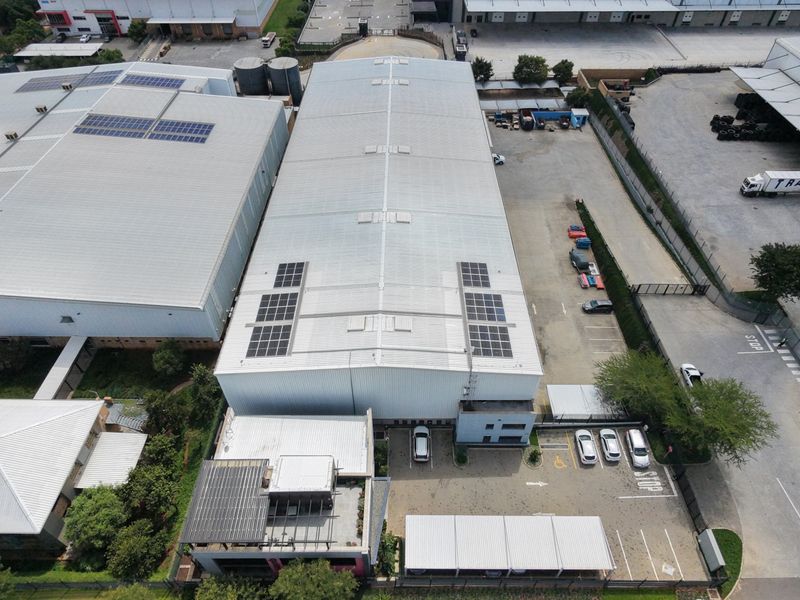 Aerial view of an industrial property featuring a large warehouse with solar panels, paved parking area, and covered parking bays.