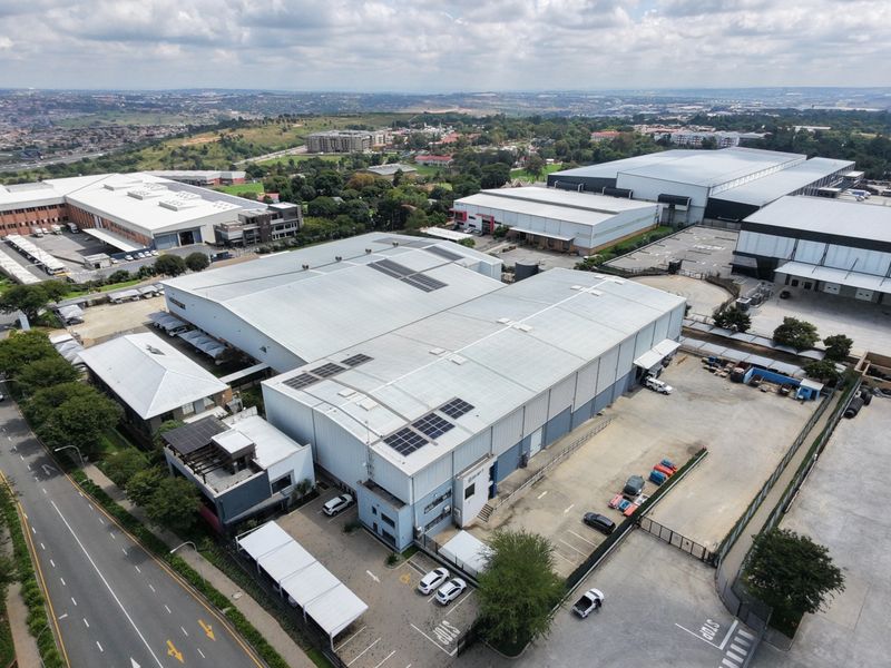 Aerial view of a large industrial warehouse complex featuring extensive roof space, solar panel installations, loading bays, and paved parking facilities.