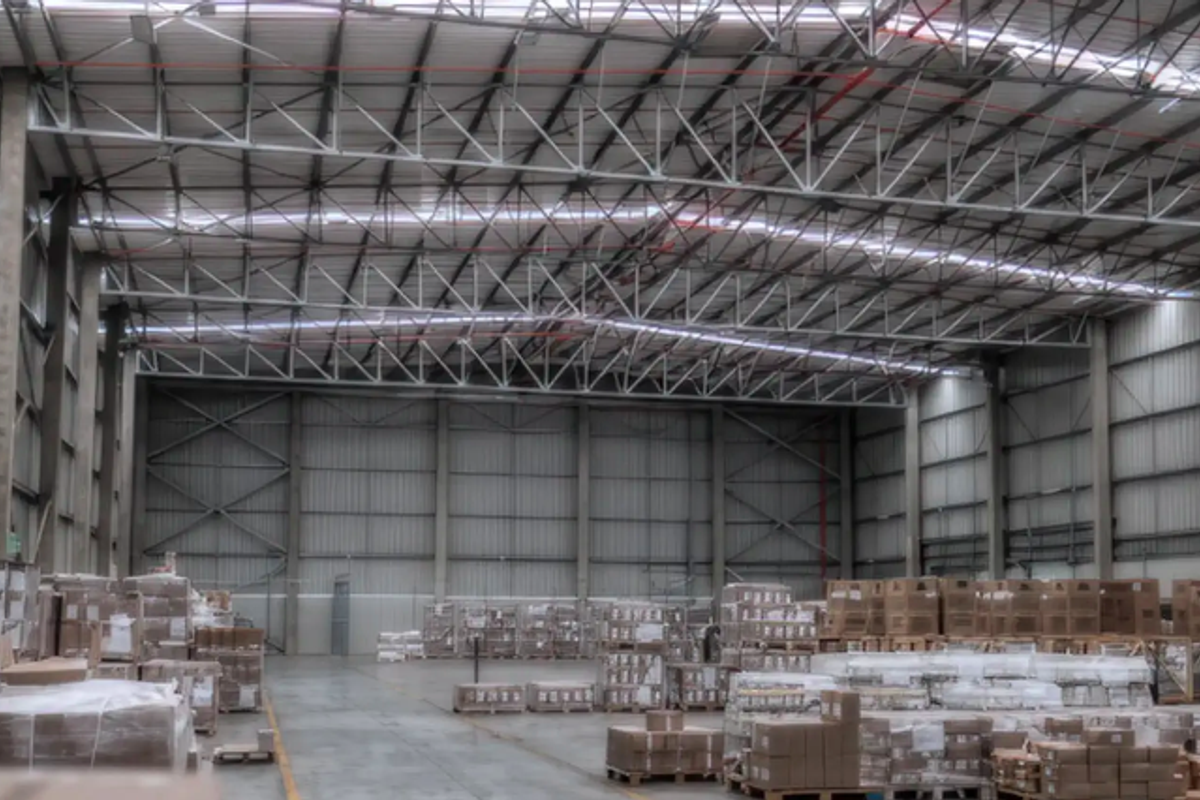 Spacious industrial warehouse featuring high ceilings with exposed steel trusses, corrugated metal walls, and durable concrete flooring, suitable for storage or manufacturing operations.