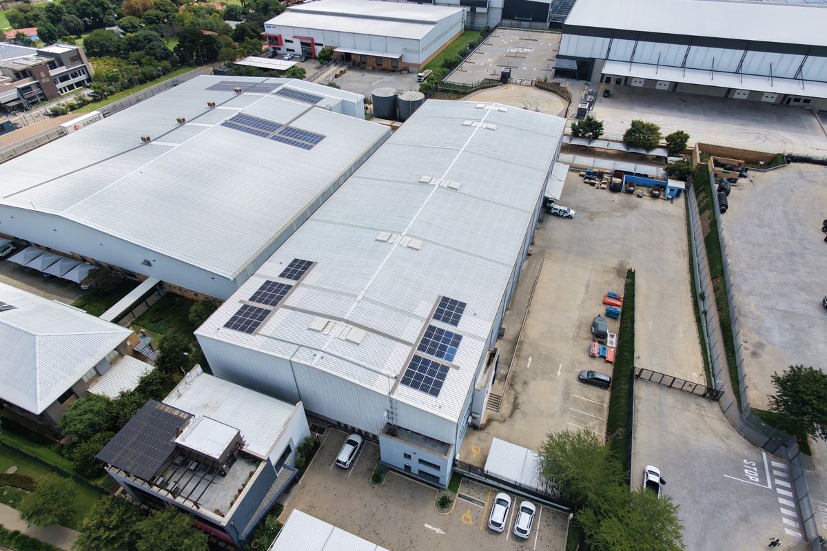 Aerial view of an industrial property featuring large warehouse buildings with solar panel installations, paved parking areas, and secure perimeter fencing.