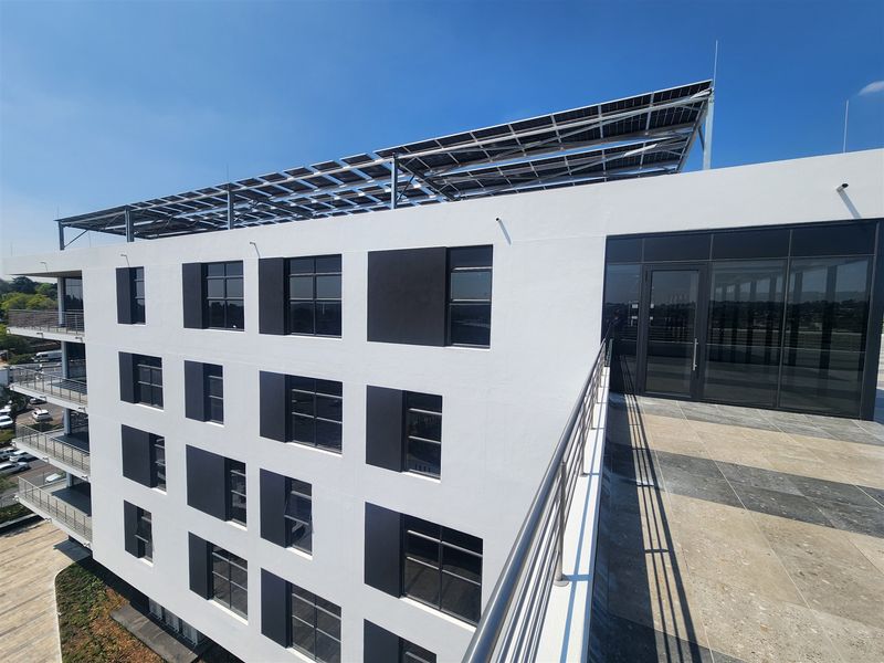 Modern office building exterior featuring a rooftop terrace with solar panels, glass doors, and contemporary architectural finishes.