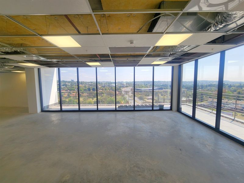 An open-plan office space featuring floor-to-ceiling windows with expansive views, a balcony, and an unfinished ceiling and floor ready for custom fit-out.