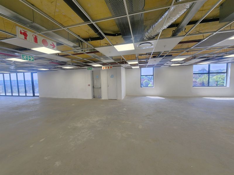 Spacious open-plan office area featuring an industrial-style exposed ceiling, concrete flooring, and large windows providing ample natural light.