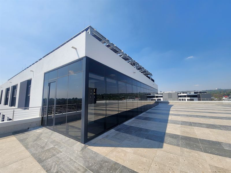 A modern rooftop terrace featuring tiled flooring, a glass-enclosed office structure, and integrated solar panels on the roof.