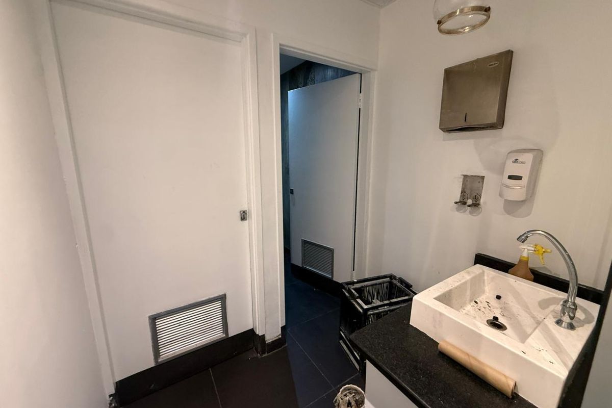 A functional retail washroom area featuring a built-in vanity with a basin, wall-mounted soap dispenser, and paper towel holder.