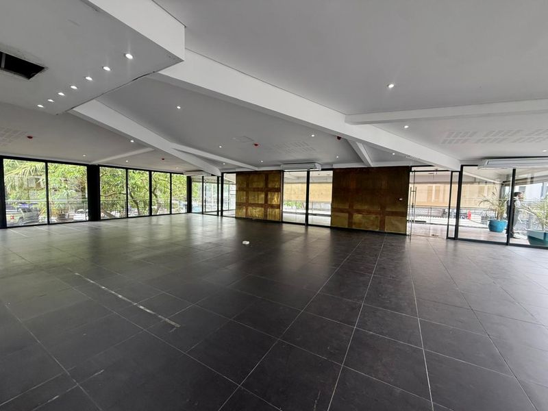 Spacious open-plan retail area featuring large floor-to-ceiling glass windows, dark tiled flooring, and modern recessed ceiling lighting.