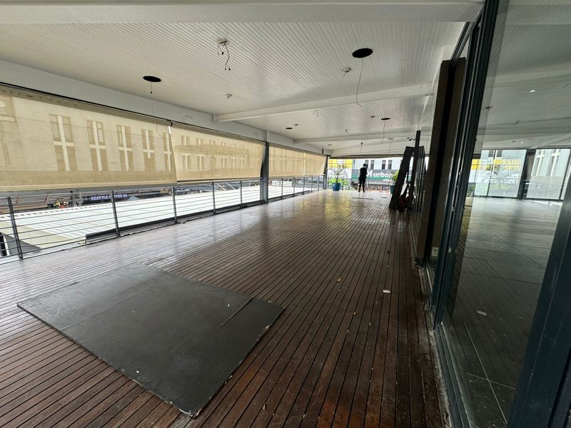 A spacious covered outdoor balcony featuring timber decking, metal railings, and retractable sun blinds, offering an open-air area suitable for retail or commercial use.