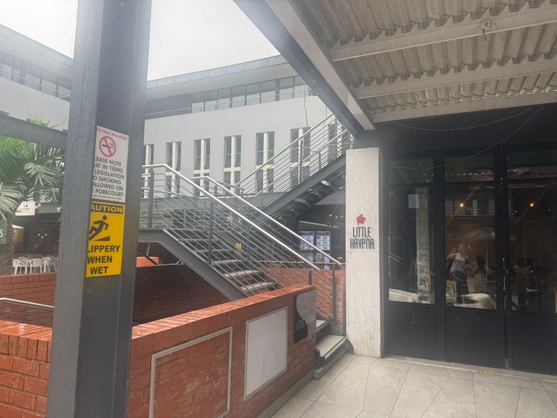 Exterior view of a commercial retail entrance featuring a brick retaining wall, metal staircase, and glass storefront facade.