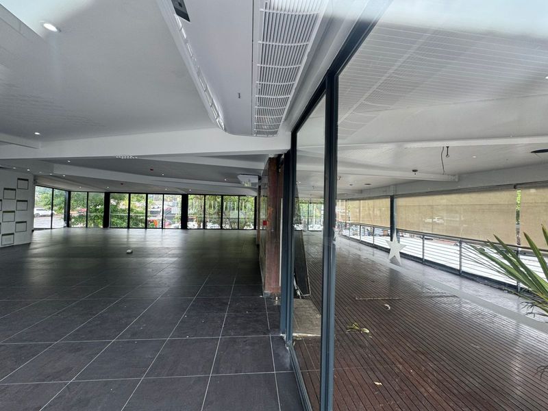Spacious open-plan retail area featuring large glass windows, dark tiled flooring, and an adjoining covered wooden deck with integrated ceiling air conditioning units.