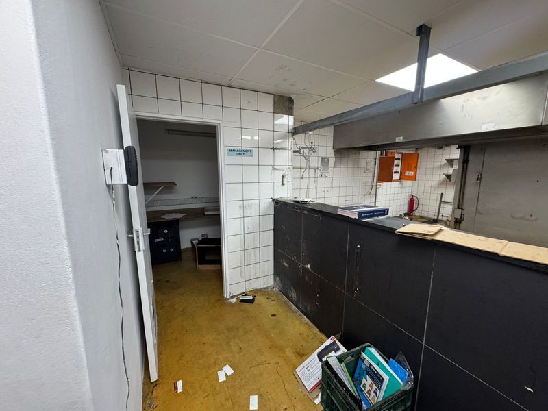 A commercial kitchen prep area featuring tiled walls, a stainless steel extractor hood, and an adjacent utility room with built-in shelving.