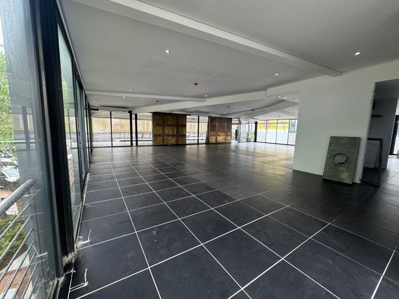 Spacious open-plan retail area featuring large glass windows, dark tiled flooring, and recessed ceiling lighting, offering a versatile layout for various business needs.