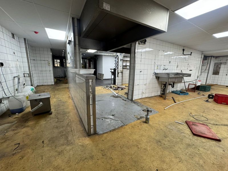 A vacant commercial kitchen space featuring tiled walls, a stainless steel sink, and an overhead extractor hood, requiring significant refurbishment.