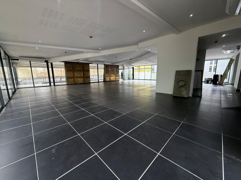 Spacious open-plan retail area featuring large glass windows, dark tiled flooring, recessed ceiling lighting, and a modern, minimalist aesthetic.