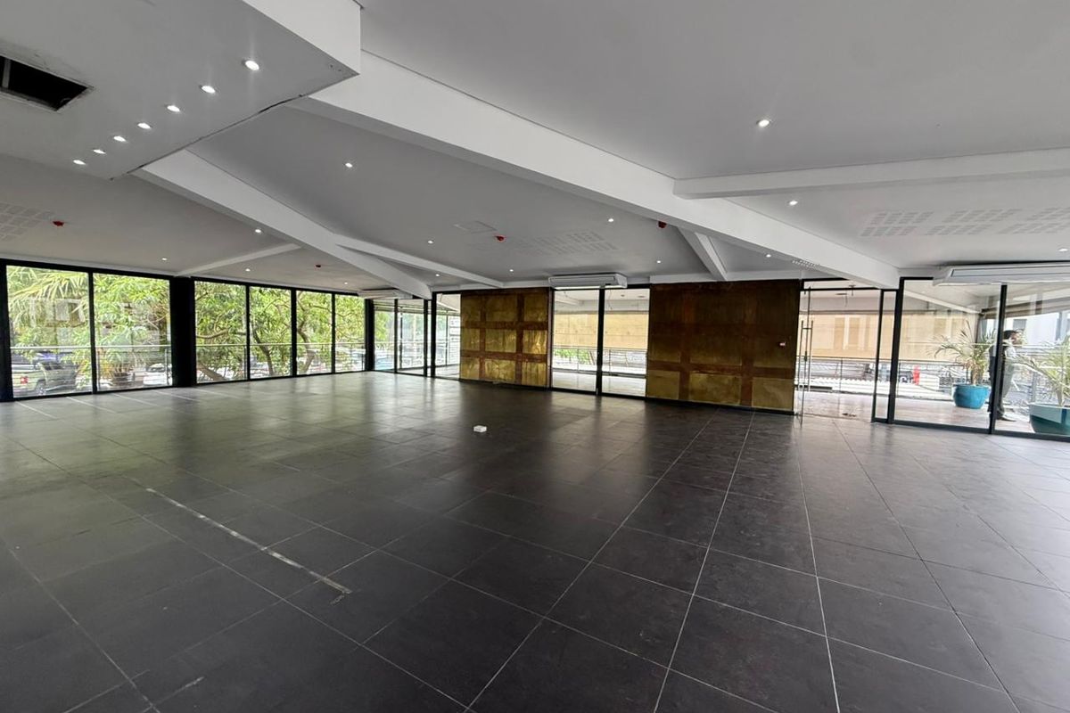 Spacious open-plan retail area featuring large floor-to-ceiling glass windows, dark tiled flooring, and modern recessed ceiling lighting.