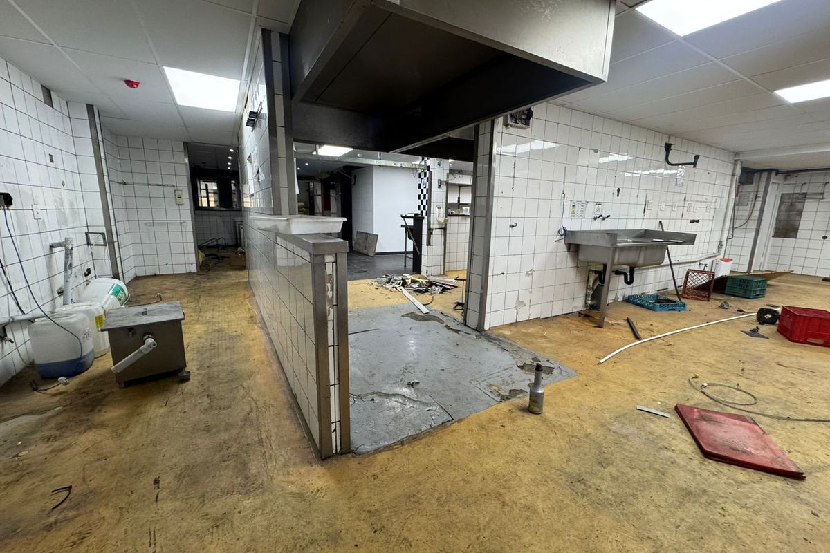A vacant commercial kitchen space featuring tiled walls, a stainless steel sink, and an overhead extractor hood, requiring significant refurbishment.