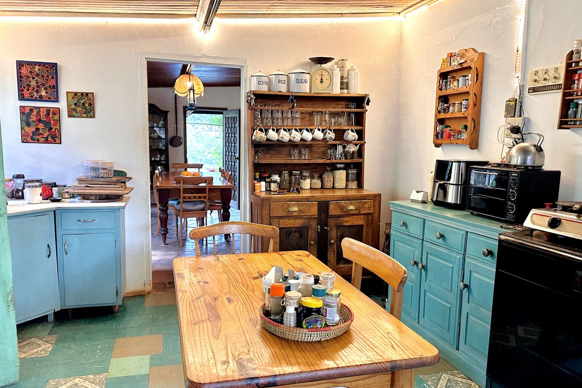 A rustic farmhouse kitchen featuring painted cabinetry, timber ceiling details, and tiled flooring, with an open transition to the adjacent dining area.