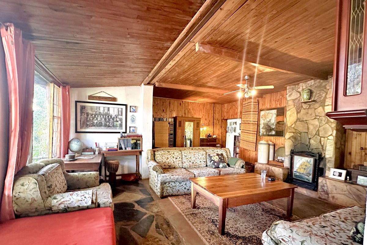 Rustic living room featuring a stone fireplace, timber-paneled walls and ceiling, and traditional flagstone flooring, offering a warm, character-filled atmosphere.
