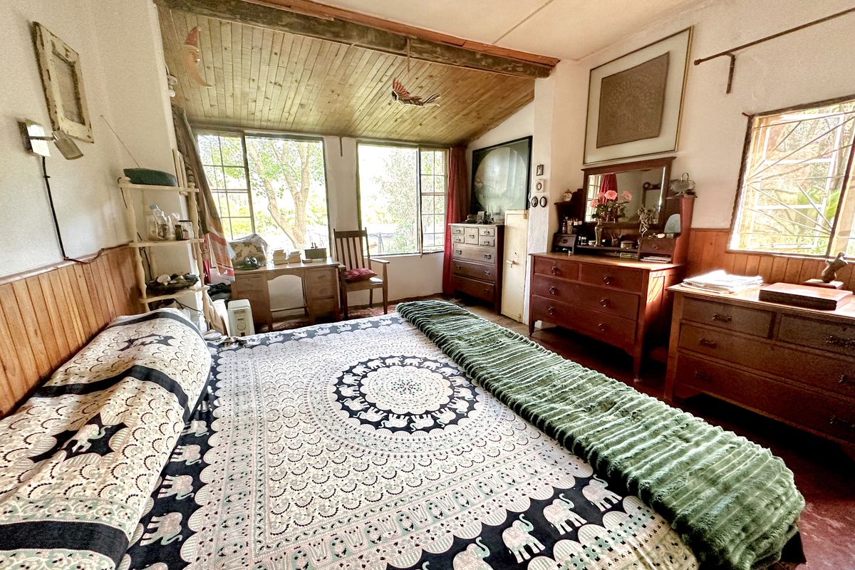 A rustic bedroom featuring timber wall paneling and a wood-paneled ceiling, with large windows providing natural light and garden views.