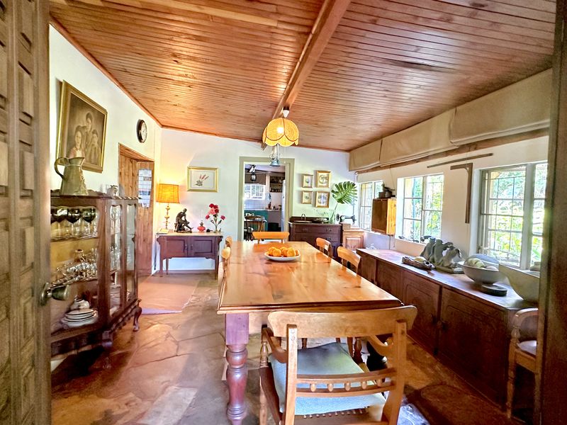A rustic dining room featuring a warm timber-clad ceiling, natural flagstone flooring, and large multi-pane windows that provide ample natural light.