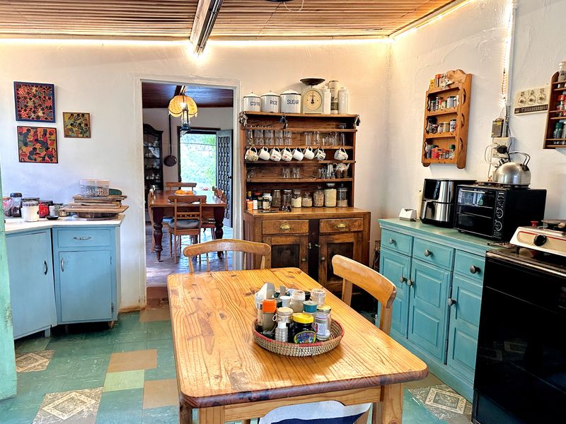 A rustic farmhouse kitchen featuring painted cabinetry, timber ceiling details, and tiled flooring, with an open transition to the adjacent dining area.