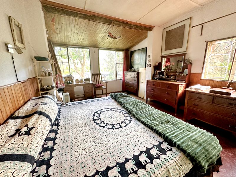 A rustic bedroom featuring timber wall paneling and a wood-paneled ceiling, with large windows providing natural light and garden views.