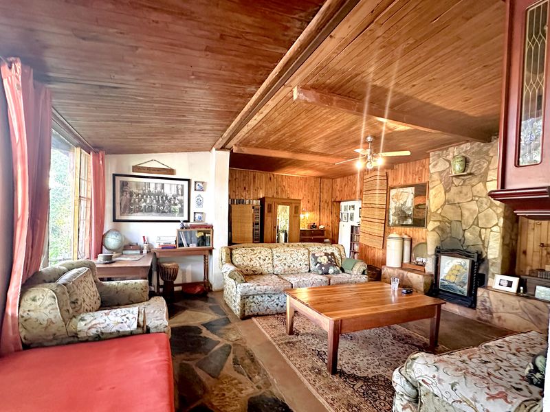 Rustic living room featuring a stone fireplace, timber-paneled walls and ceiling, and traditional flagstone flooring, offering a warm, character-filled atmosphere.
