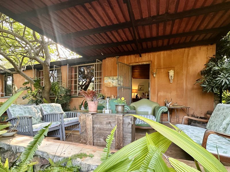 A rustic covered patio area featuring a corrugated metal roof, stone retaining wall, and direct access to the interior through a steel security gate.