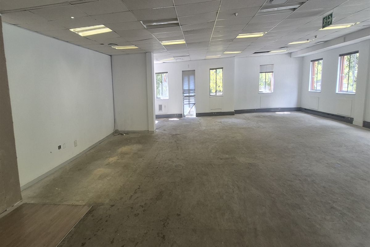 A spacious, vacant open-plan office area featuring a suspended ceiling, recessed lighting, and exposed concrete flooring, ready for custom fit-out.