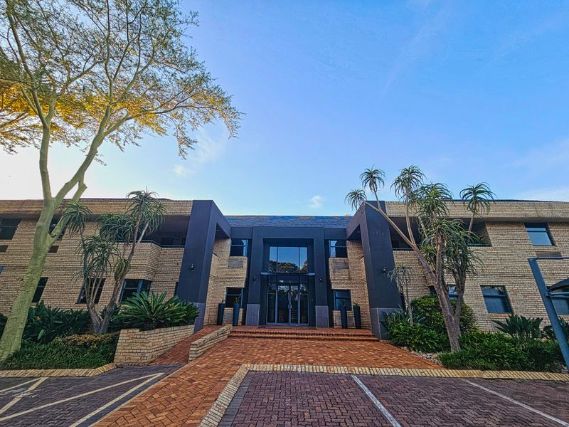 Front elevation of a professional office building featuring a brick facade, glass entrance, and paved driveway with established landscaping.