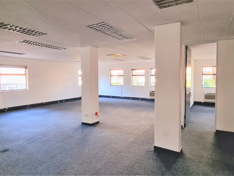 Spacious open-plan office area featuring suspended ceilings, recessed lighting, and large windows with security bars, providing a versatile workspace.