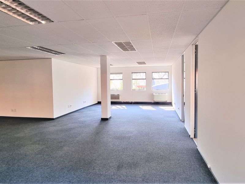 A spacious, open-plan office area featuring a suspended ceiling, recessed lighting, and carpeted flooring, providing a versatile workspace ready for configuration.