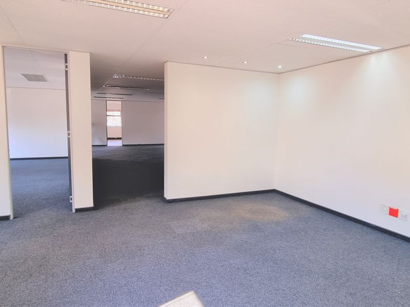 A vacant, open-plan office space featuring neutral walls, carpeted flooring, and recessed ceiling lighting, offering a clean and functional workspace.