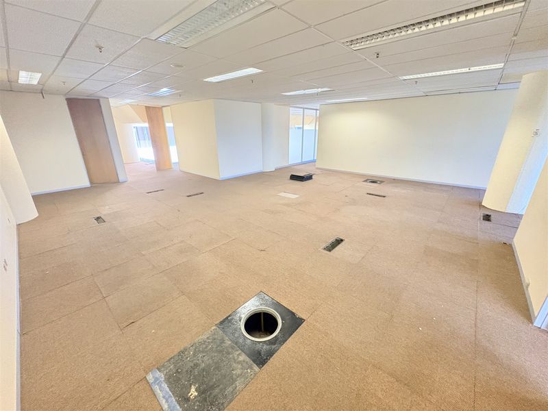 An open-plan office space featuring a suspended ceiling, recessed lighting, and a raised access floor with multiple floor-mounted electrical service points.