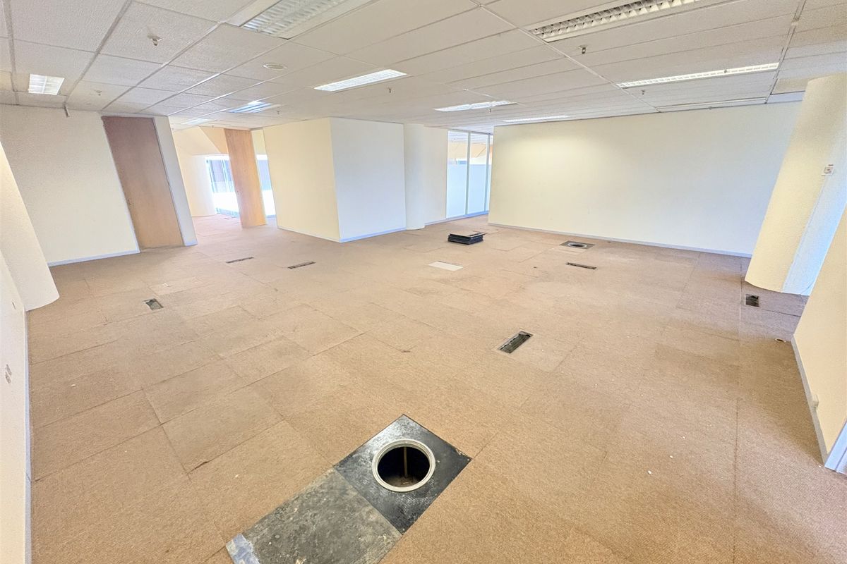 An open-plan office space featuring a suspended ceiling, recessed lighting, and a raised access floor with multiple floor-mounted electrical service points.