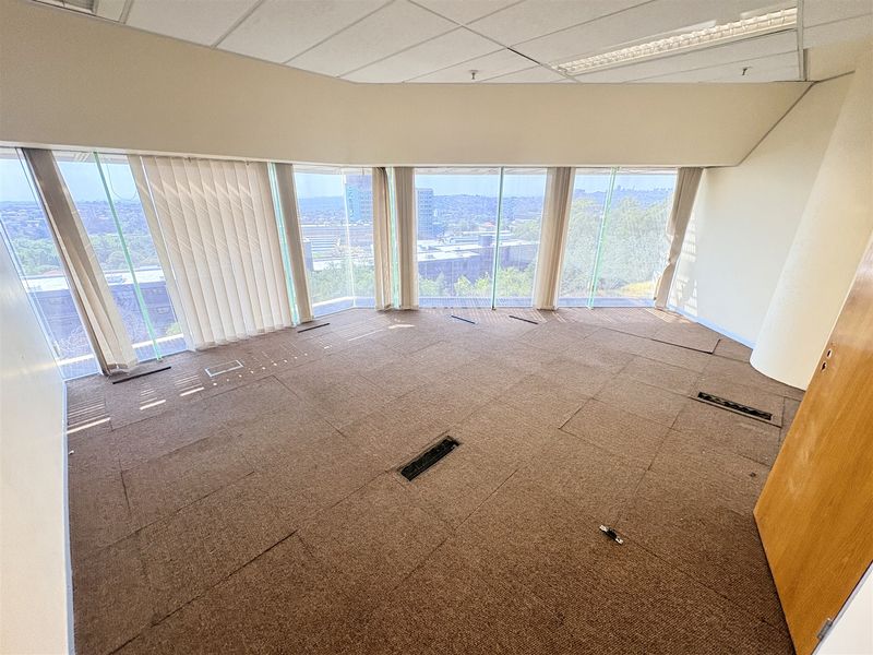 Empty office space featuring floor-to-ceiling windows with panoramic views, suspended ceiling, and carpeted flooring with integrated electrical access points.