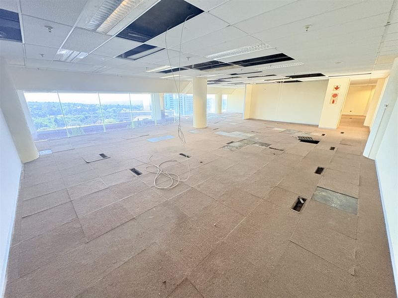 Open-plan office space featuring floor-to-ceiling windows with city views, requiring ceiling and flooring repairs to restore functionality.