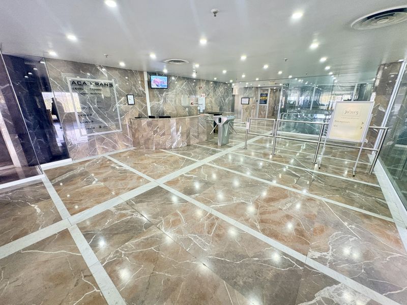 A professional office building lobby featuring polished marble flooring, marble wall cladding, a reception desk, and security turnstiles for controlled access.