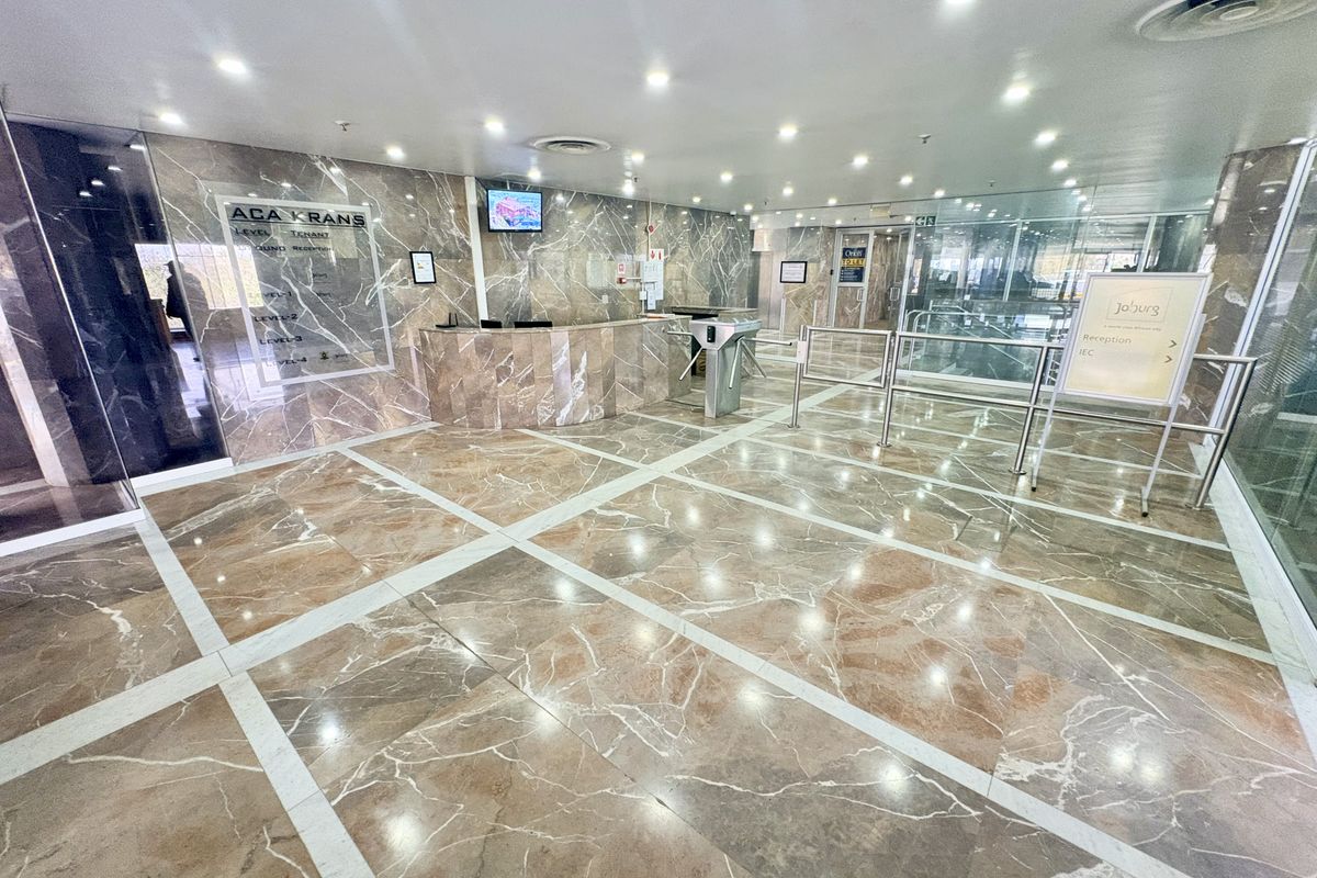 A professional office building lobby featuring polished marble flooring, marble wall cladding, a reception desk, and security turnstiles for controlled access.