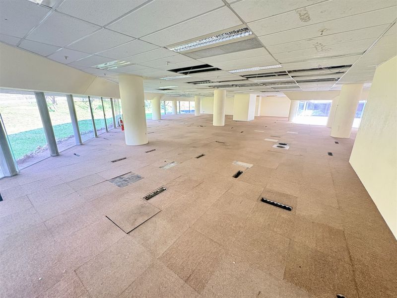 Spacious open-plan office area featuring floor-to-ceiling windows, structural columns, and a suspended ceiling, currently in need of refurbishment.