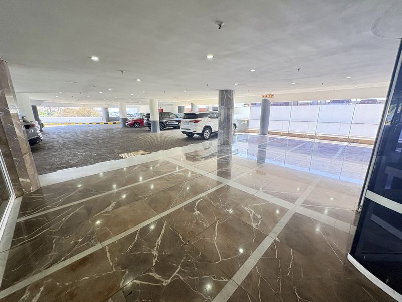 A spacious, well-lit indoor parking garage featuring polished marble flooring, structural columns, and a modern glass partition wall.