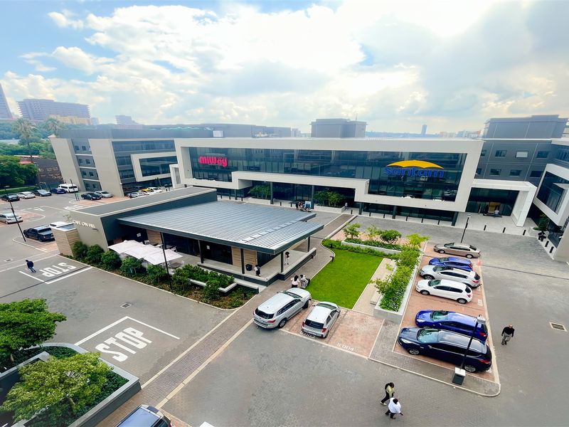 Aerial view of a modern commercial office complex featuring landscaped gardens, paved parking facilities, and contemporary glass and metal building architecture.